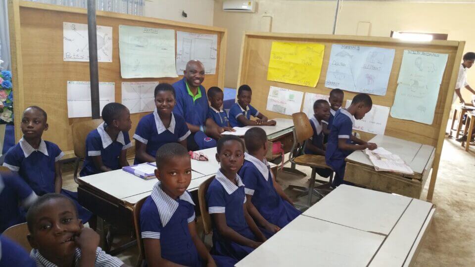 John Sagoe Sitting With Students In Class First Building